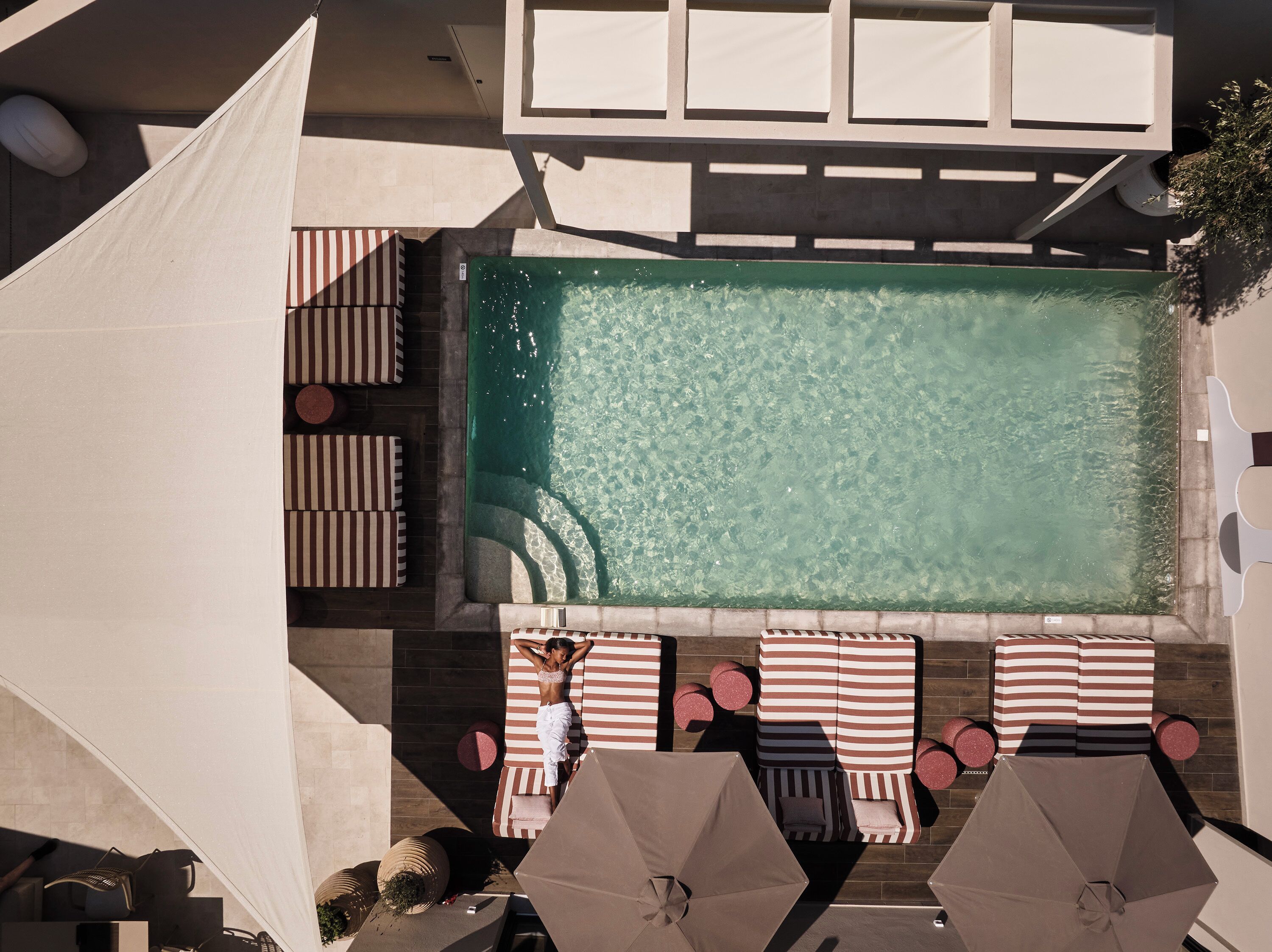 Un área de piscina en la azotea con sillones de baño a rayas y sombrillas.