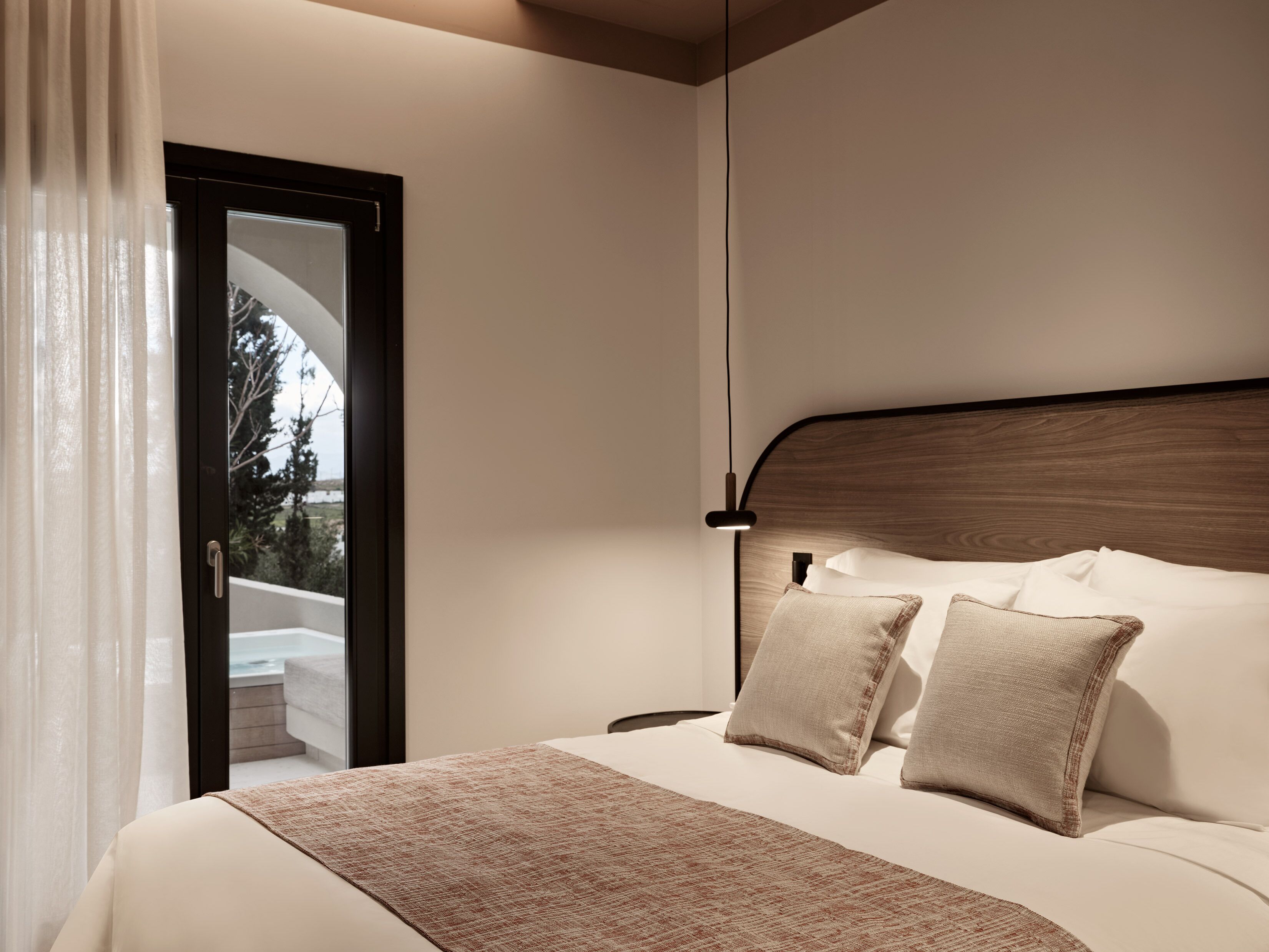 A bedroom with a bed, pillows, a bedside table, a lamp, and a view through a door.