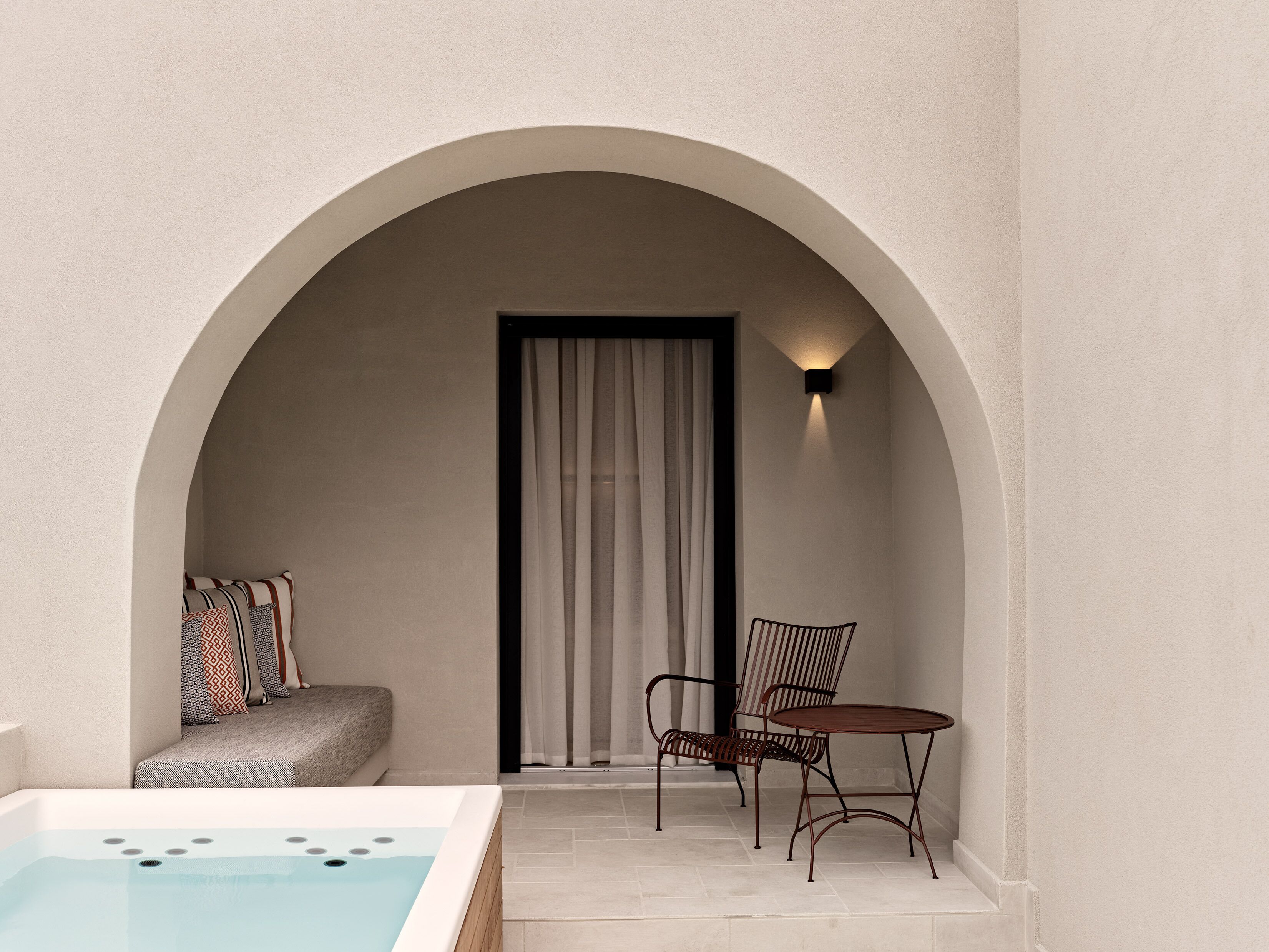 A spa area with a hot tub, two chairs, a cushioned bench, and a curtain.