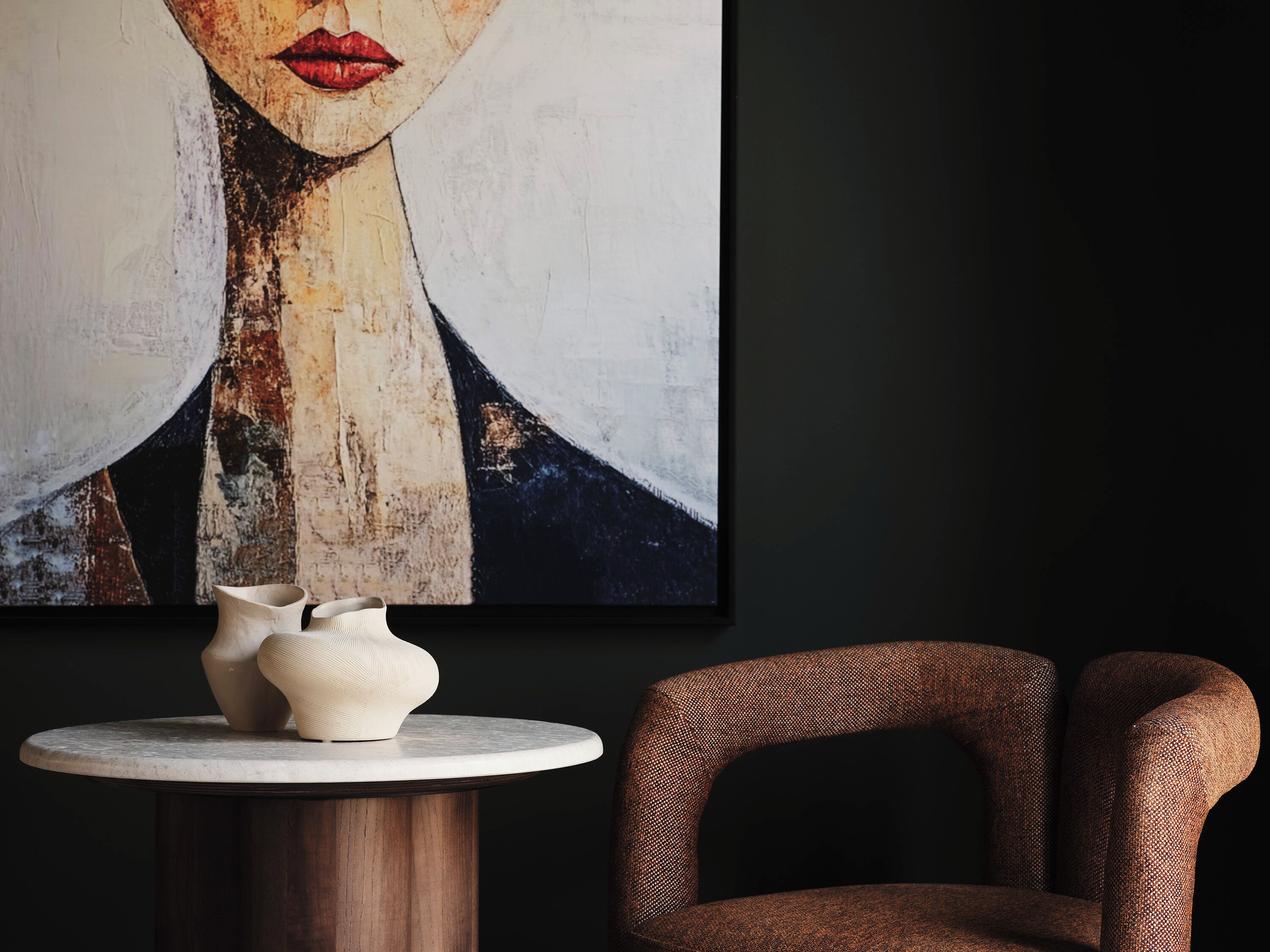 Een modern interieur met een ronde houten tafel, een stoel met een reliëf oppervlak in bruin, en een groot abstract schilderij aan de muur.