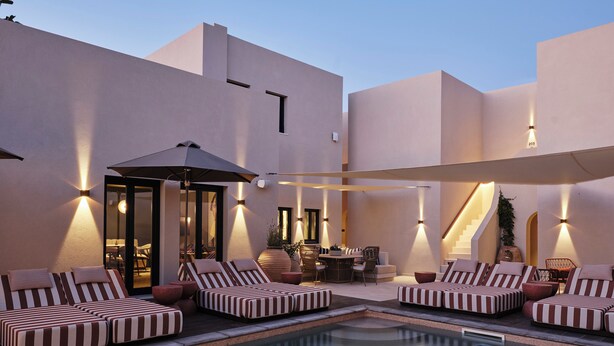 Zona de piscina con sillones a rayas, una mesa de comedor y una escalera.