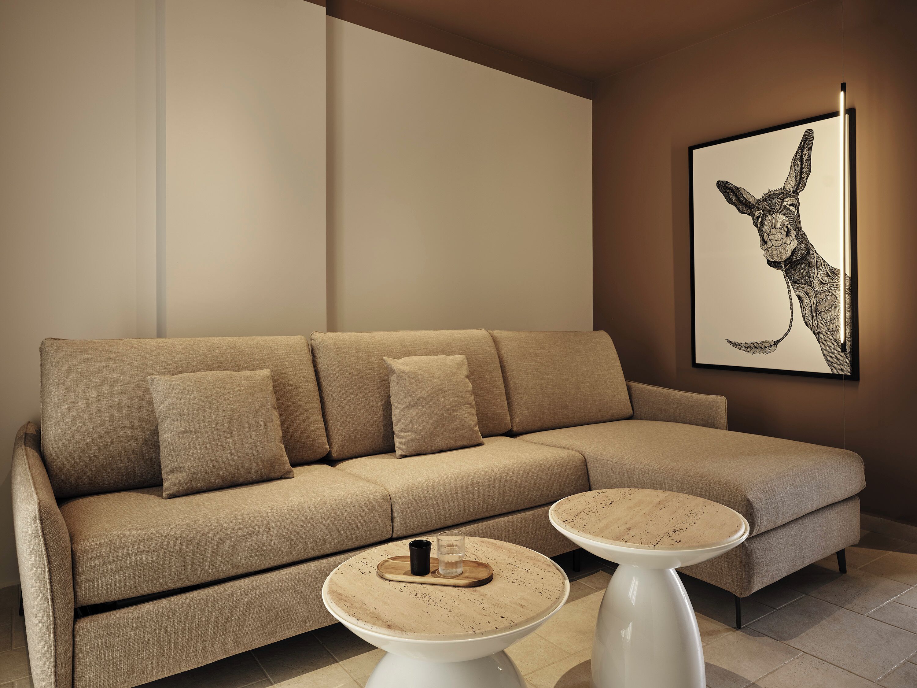 A modern living room with a beige sectional sofa, two round coffee tables, and a framed artwork on the wall.