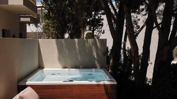 Un jacuzzi con escalones de madera y cojines a rayas, rodeado de árboles y un edificio.