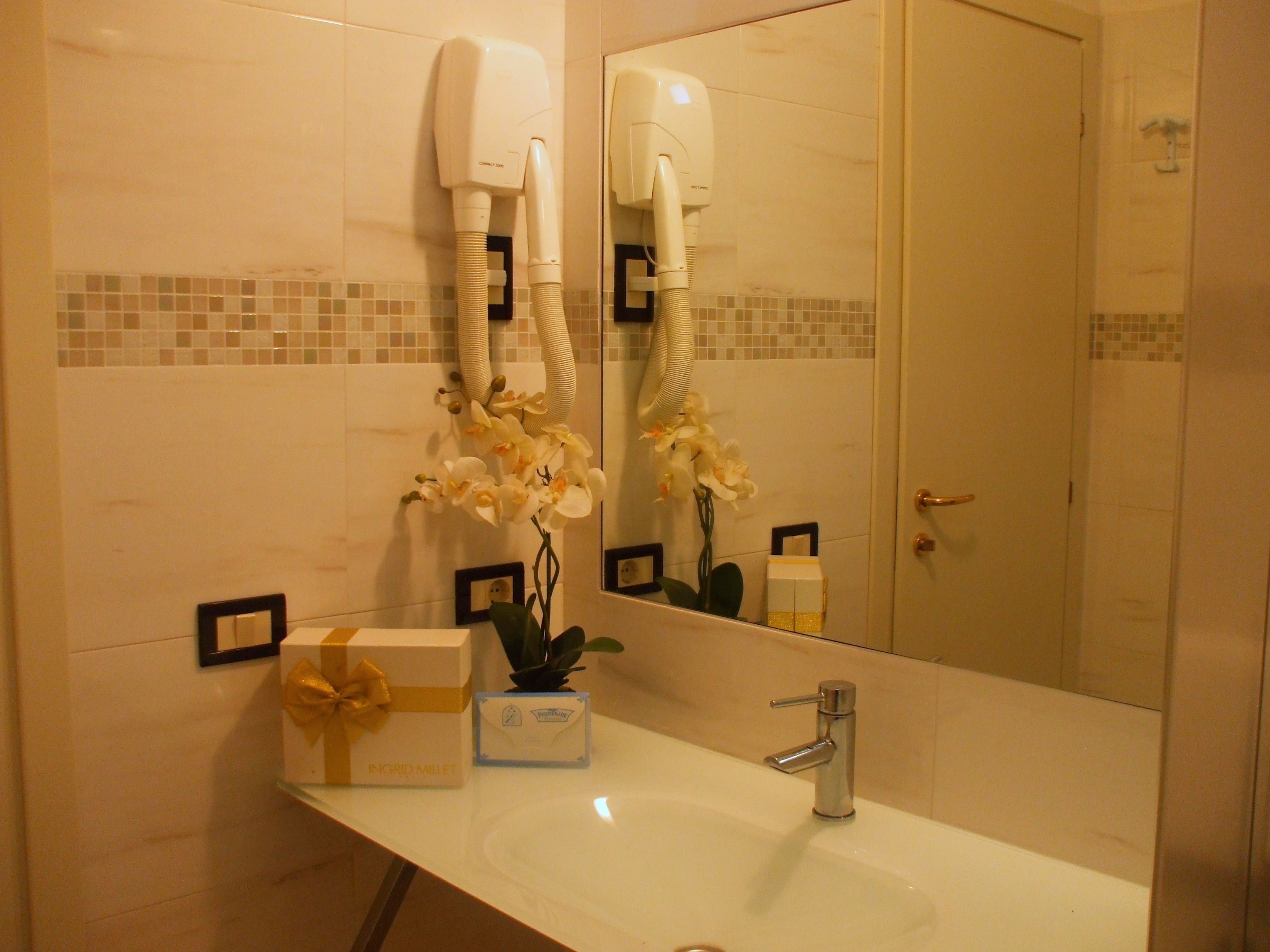 A bathroom with a white sink, a mirror, a hairdryer, a gift box, and a small plant.