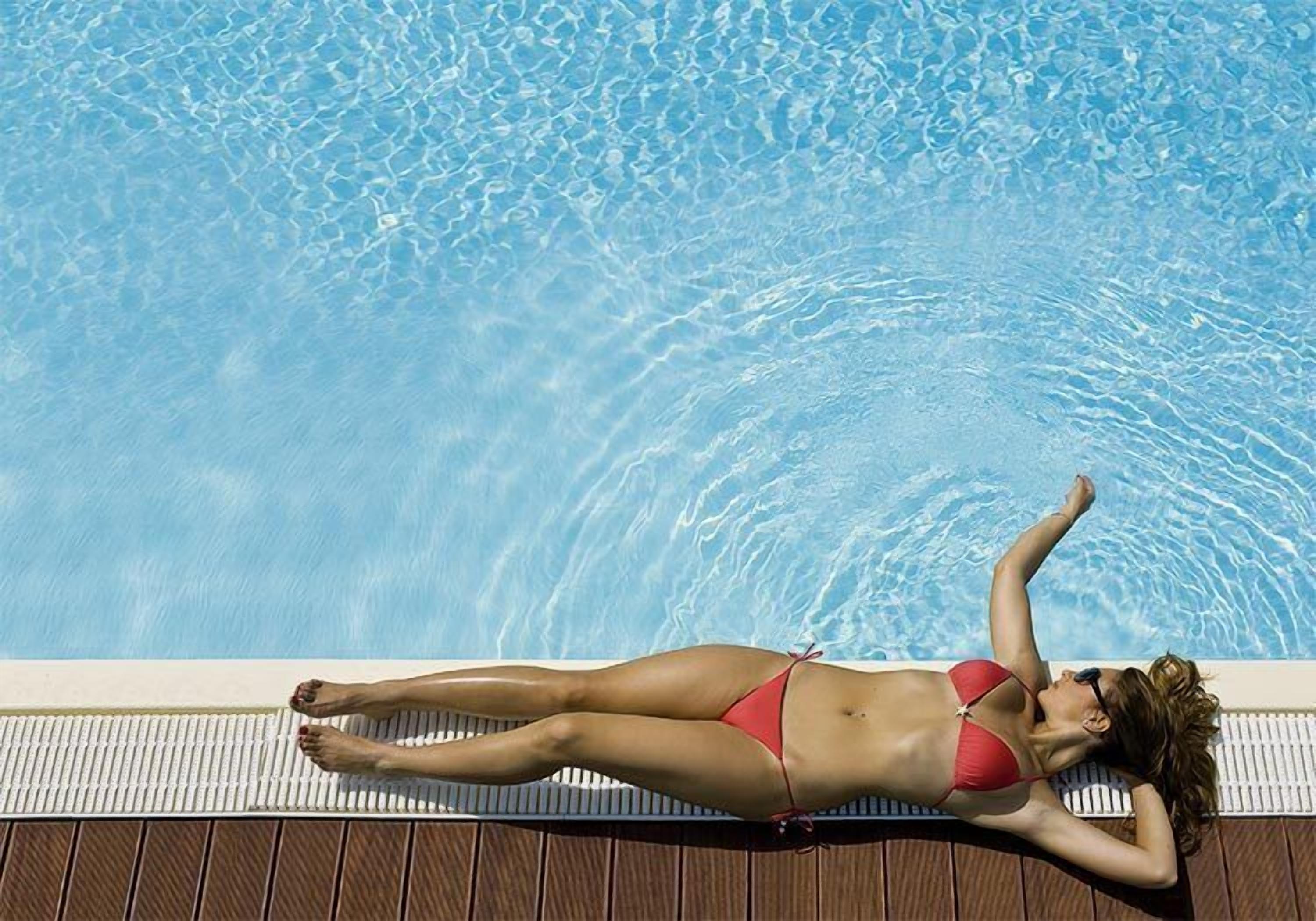 Una persona recostada en una silla de piscina junto a una alberca.