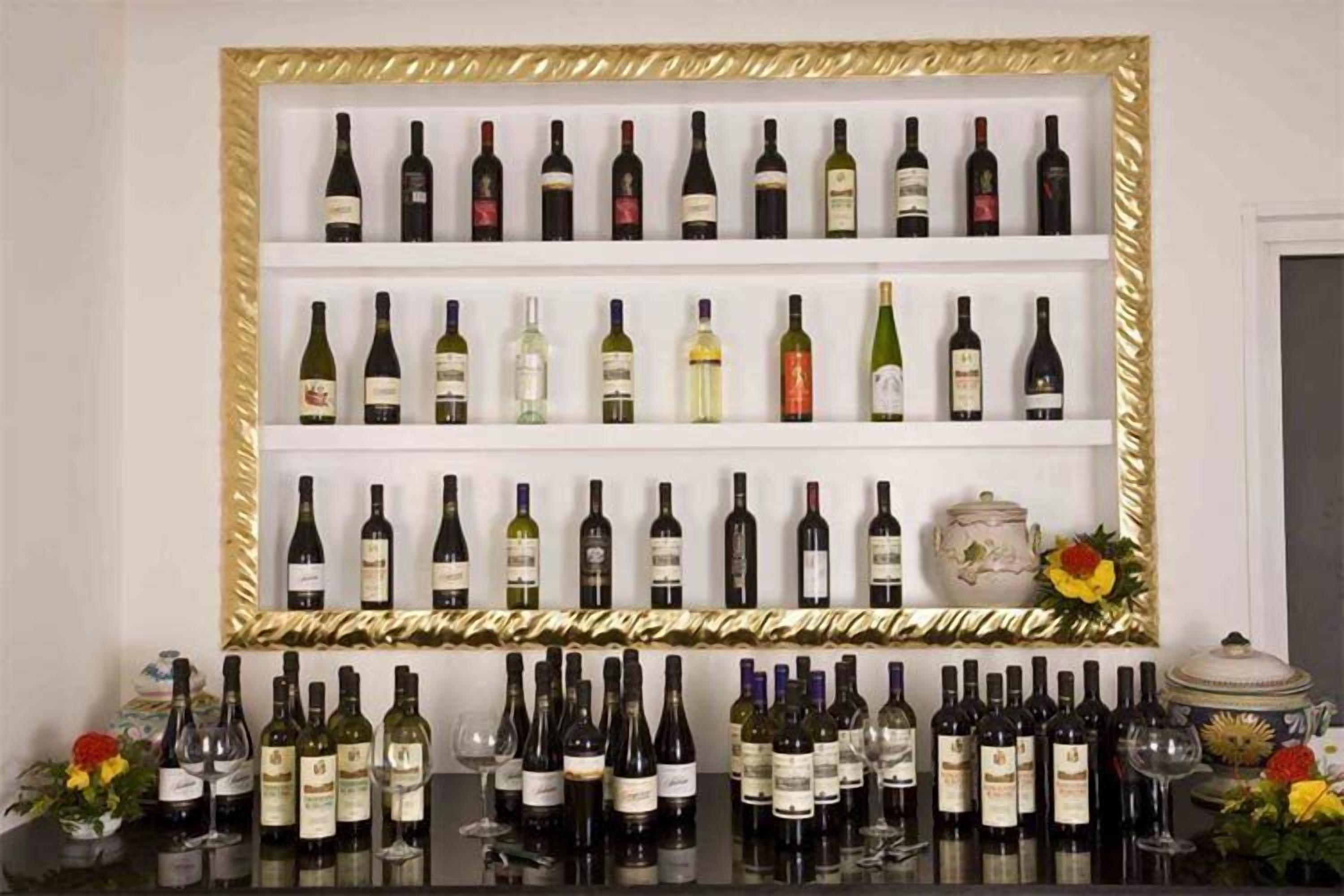 A wall of wine bottles in a gold-framed display case.