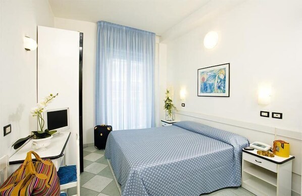 A hotel room with a bed, a desk with a computer, a chair, a suitcase, and a window with curtains. - Hotel Elite (Cattolica)