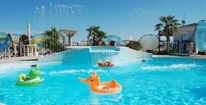 A swimming pool with inflatable toys, palm trees, and a clear sky. - Hotel Elite (Cattolica)