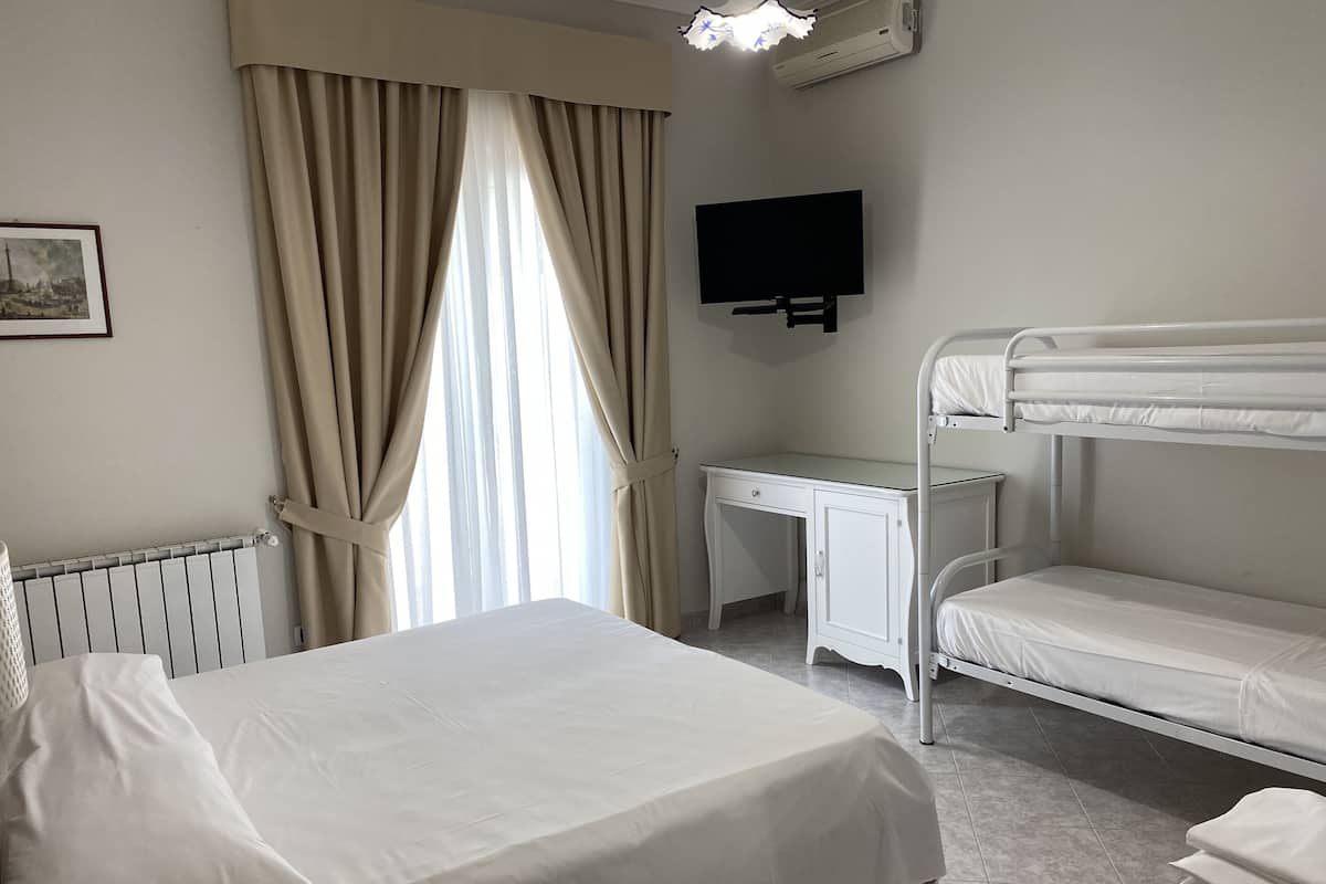Ein Hotelzimmer mit einem Etagenbett, einem Schreibtisch, einem Stuhl, einem Flachbildfernseher und einer Heizung.