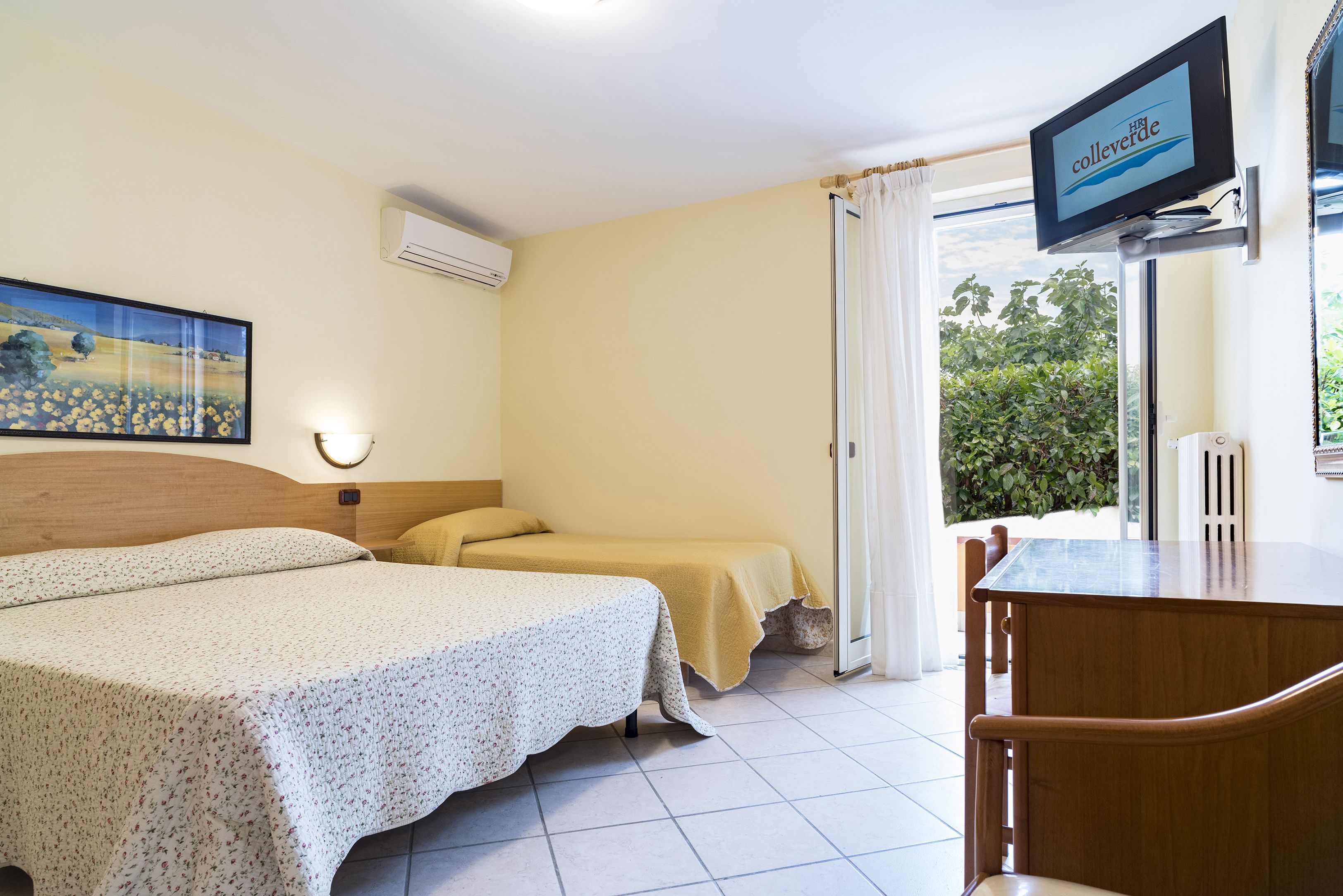 Una camera d'albergo con un letto, un tavolino, una televisione e una finestra con tende.
