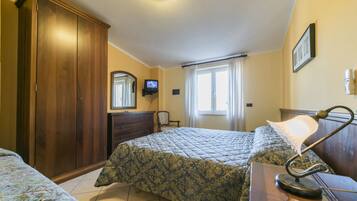 Ein Schlafzimmer mit zwei Betten, einem Kleiderschrank, einem Schreibtisch mit Lampe, einem Fernseher und einem Fenster mit Vorhängen.