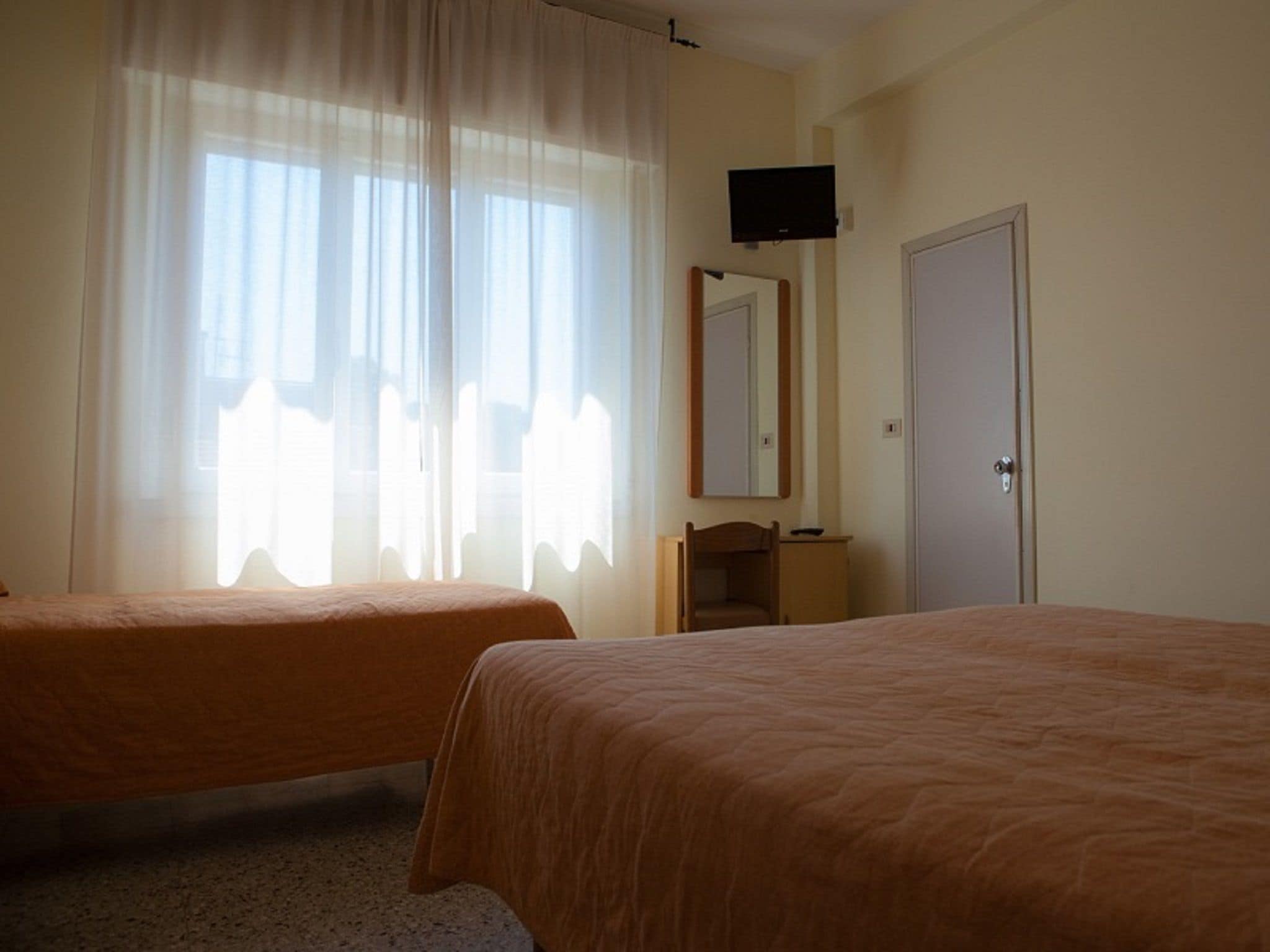A hotel room with two single beds, a television mounted on the wall, a mirror above a wooden dresser, and a door to the right.