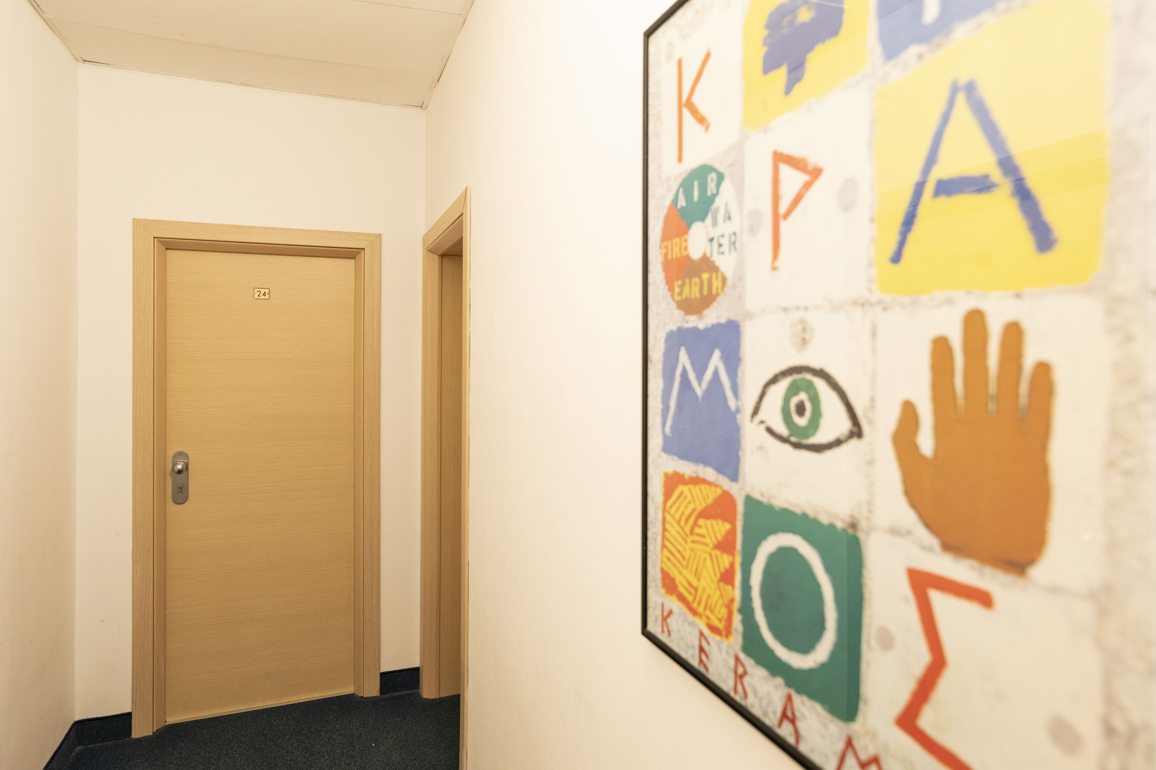 A hallway with a wooden door labeled '24' and a wall with colorful educational posters.