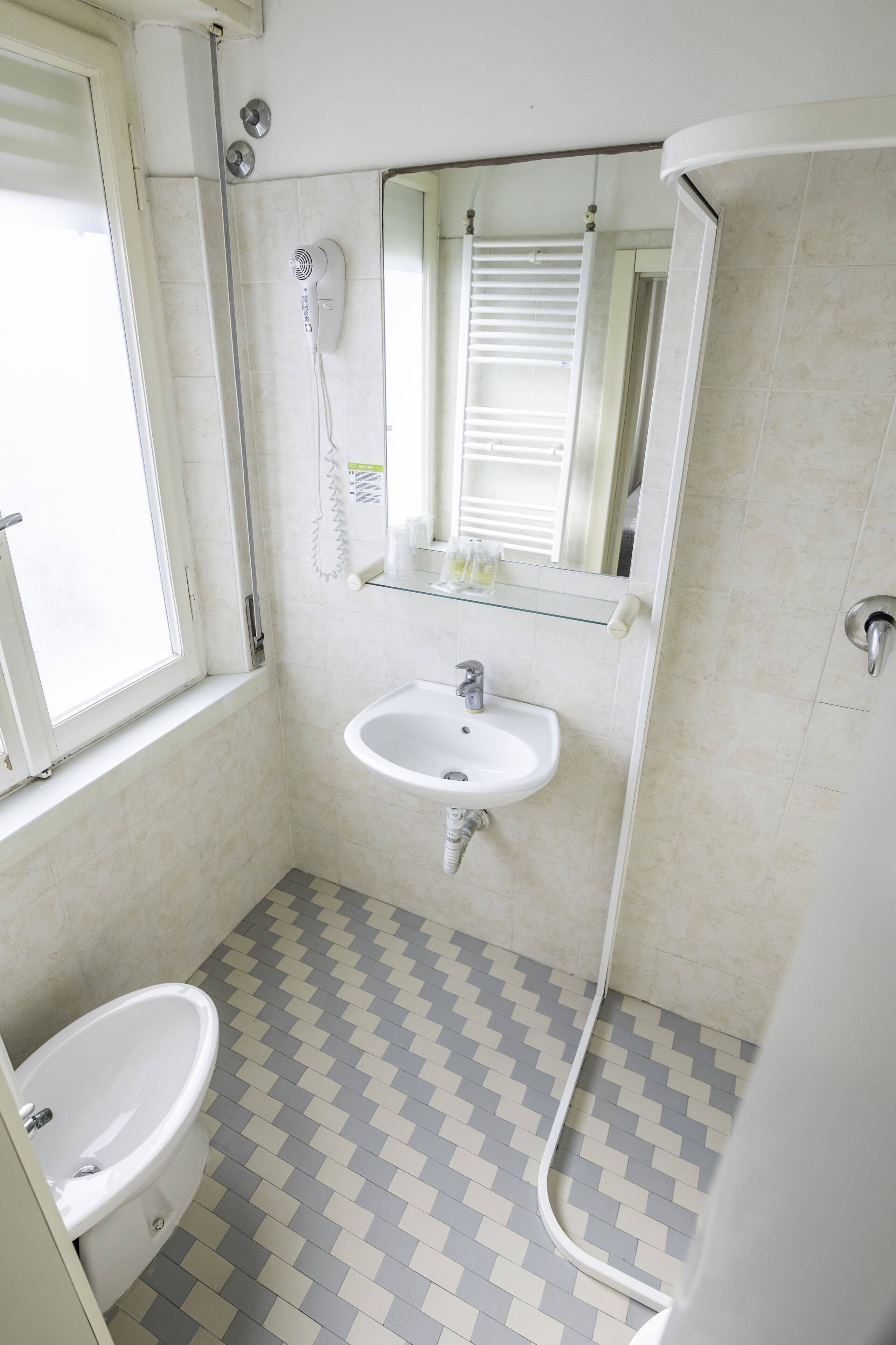 A small bathroom with a sink, a mirror, a window, and a shower.