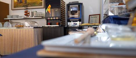 A kitchen area with a coffee machine, a food display, and a table with a placemat.