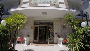 Ein Hotel Eingang mit einem Schild, auf dem 'Ausonia' steht und die Zahl '51' über der Tür angebracht ist. An beiden Seiten des Eingangs befinden sich Kübelpflanzen.