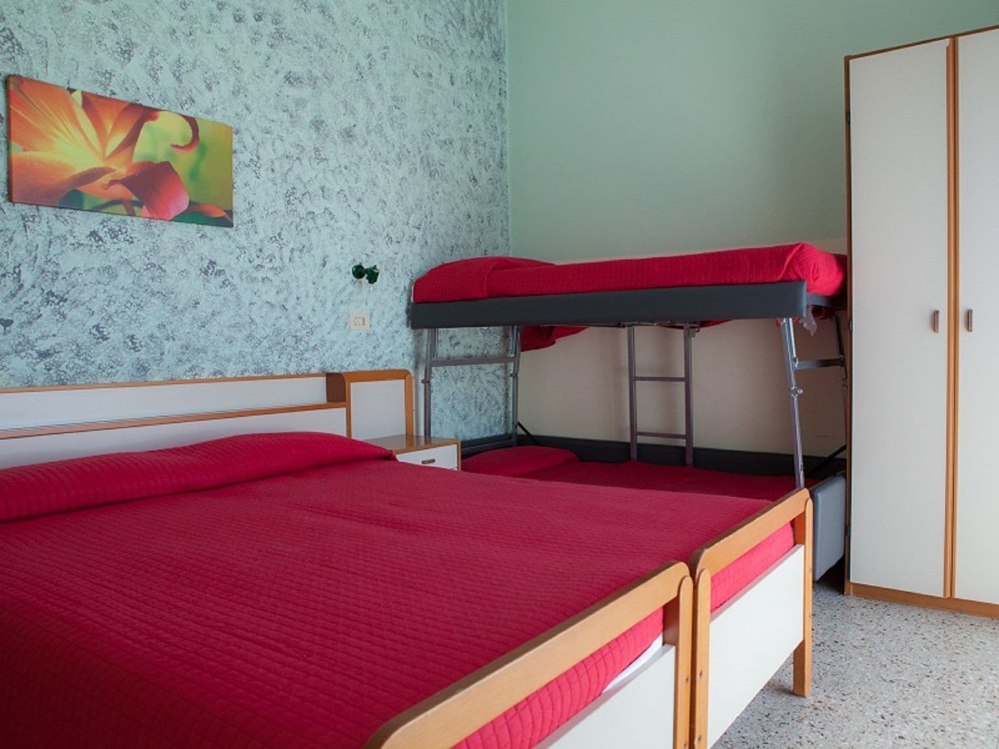 Habitación con literas, una colcha roja, cabecero de madera, una pequeña escalera y un armario.