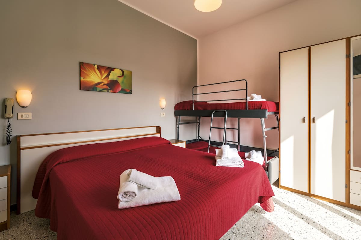 Ein Hotelzimmer mit einem großen Bett, einem Stockbett, einem Kleiderschrank und einem Bild an der Wand.