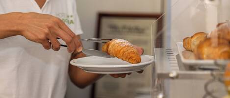 A person serving a croissant from a glass display case.