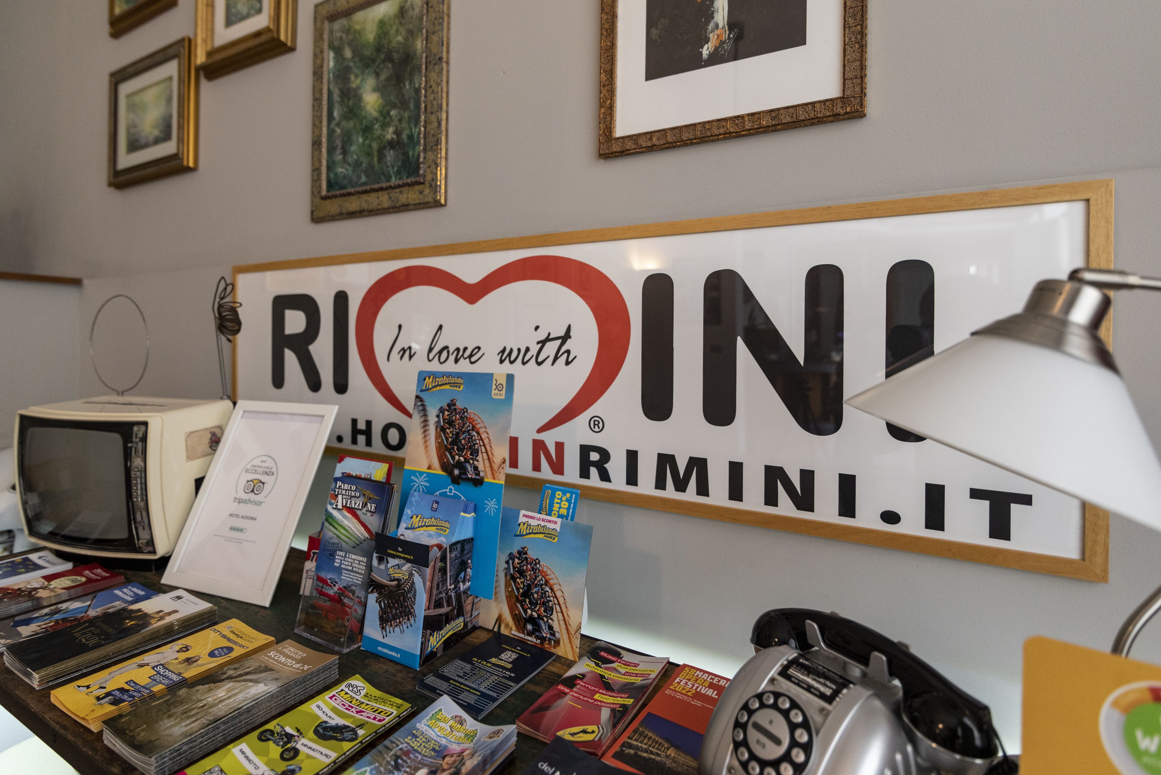 Un escritorio con un letrero que dice "In love with RIMINI.IT" y varios folletos de viaje.