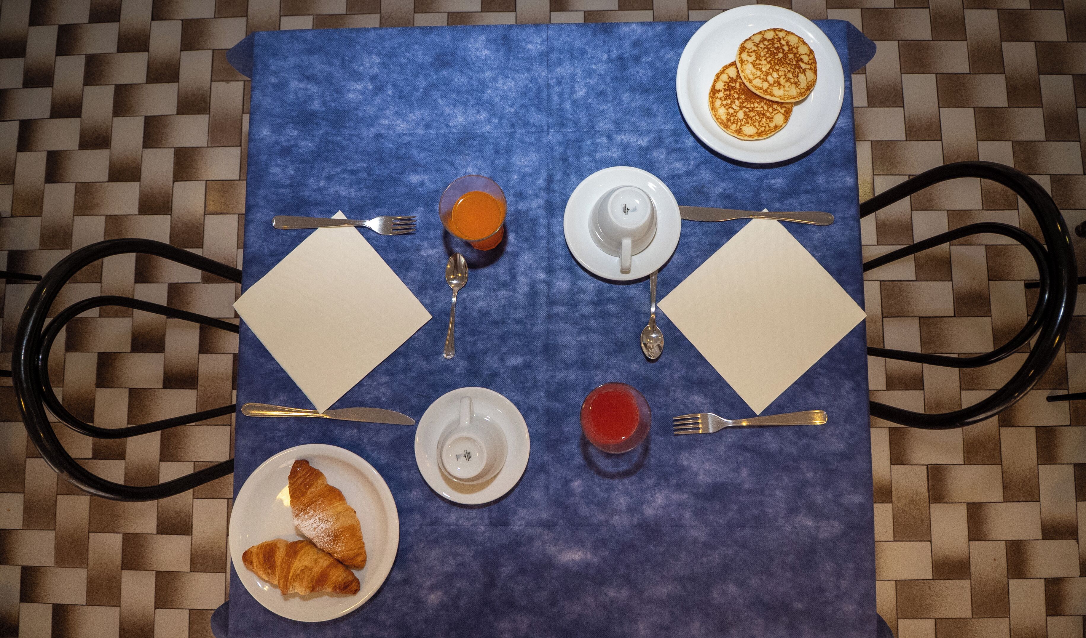 A breakfast table with croissants, pancakes, a glass of orange juice, and a glass of red juice.