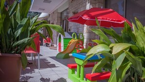 Ein Spielbereich für Kinder mit bunten Spielgeräten und einem roten Sonnenschirm.