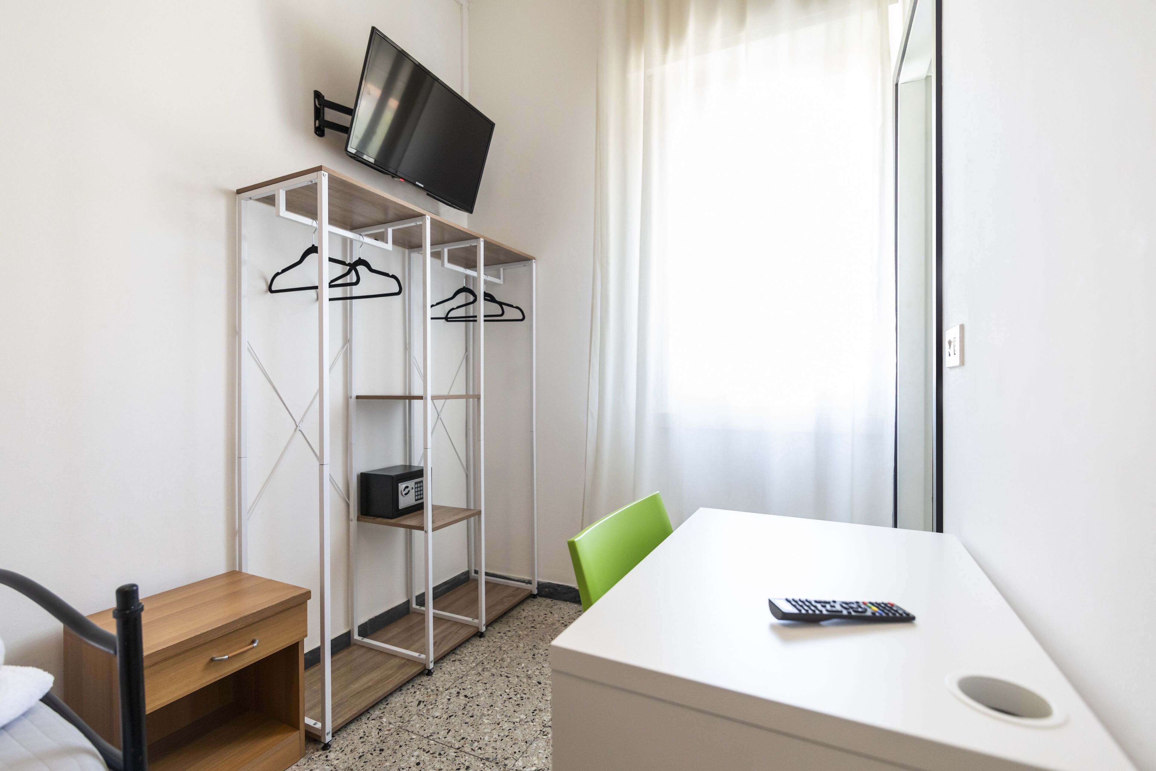 Een hotelkamer met een bed, een bureau met stoel, een televisie op een plank en een kapstok.
