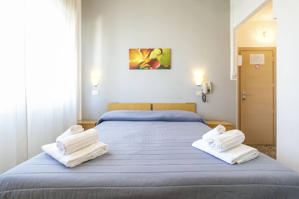 Ein Hotelzimmer mit Bett, zwei Nachttischlampen, einem Bild an der Wand und einer Tür mit einem Schild.