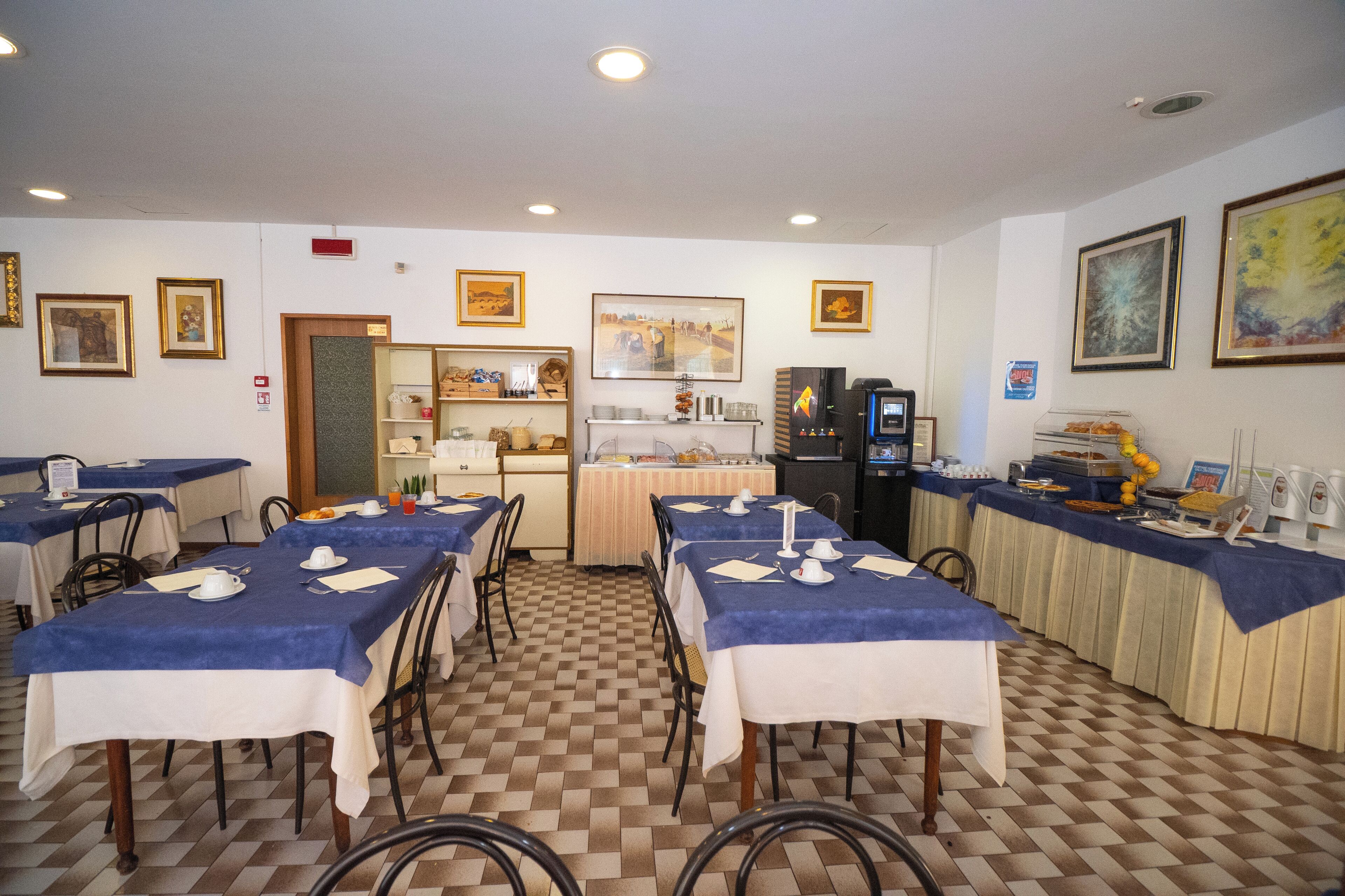 A dining area with tables set for breakfast, a buffet station, and a coffee machine.