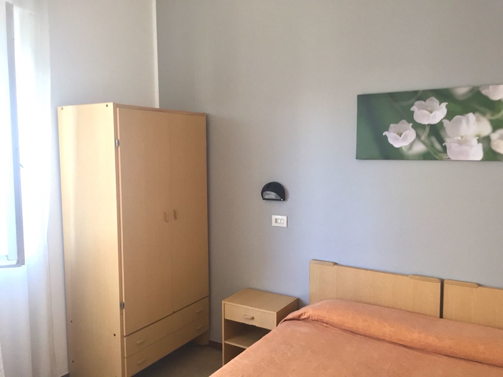 Un dormitorio con cama, mesita de noche, armario e iluminación en la pared.