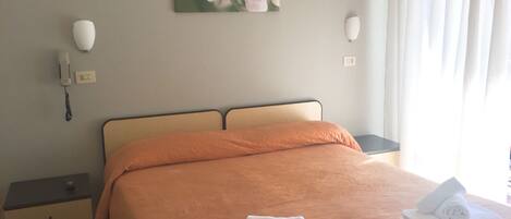 Une chambre d’hôtel avec un lit, une table de chevet, un téléphone, un tableau et une fenêtre avec des rideaux.