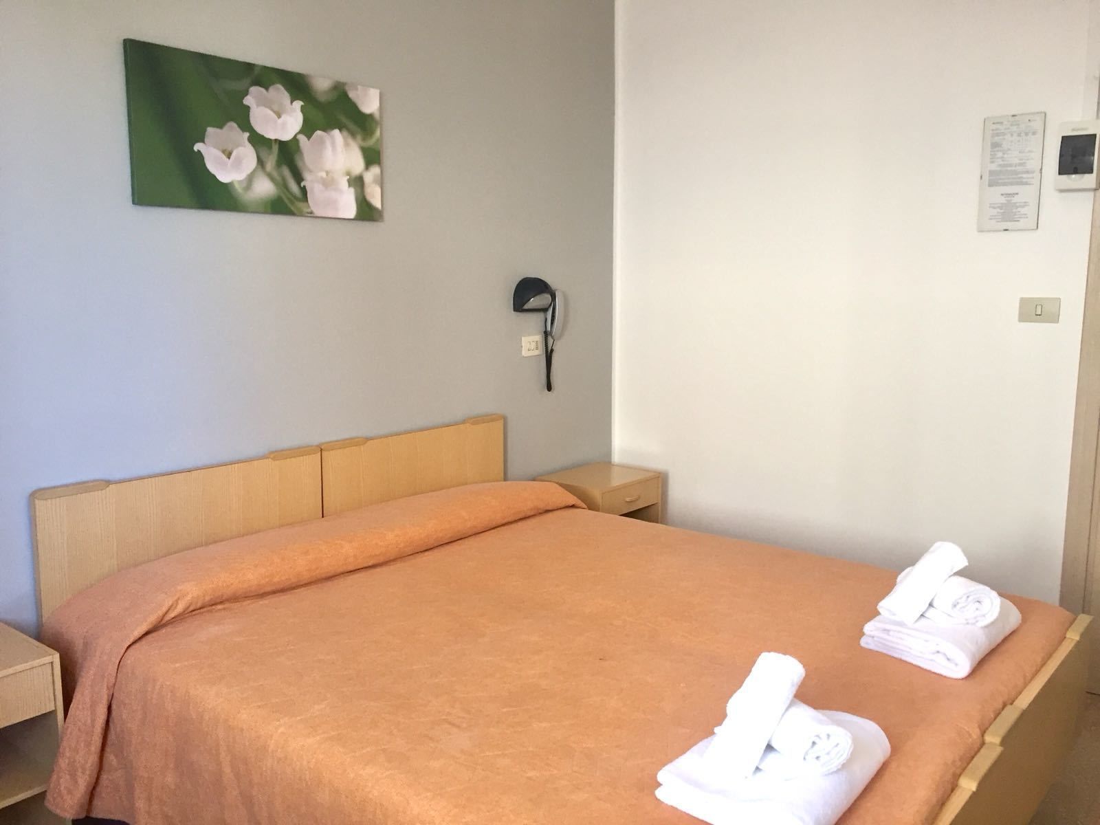 A neatly made bed with an orange bedspread and two folded white towels. A small bedside table is visible to the left of the bed.