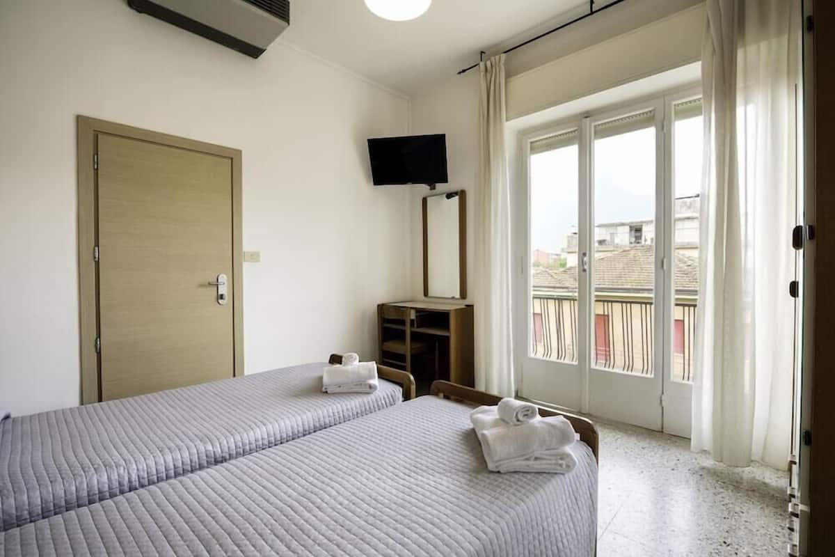 Ein Hotelzimmer mit zwei Betten, einem Fernseher, einem Balkon mit Aussicht und einer Tür.