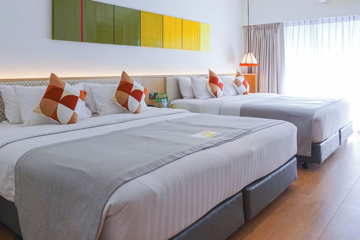 A hotel room with two beds, a bedside table, a lamp, and a wall with a geometric pattern.