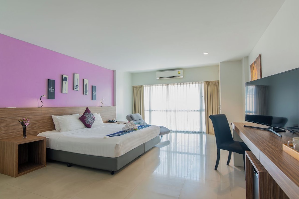 A modern hotel room with a bed, bedside table, TV, and a desk with a chair.
