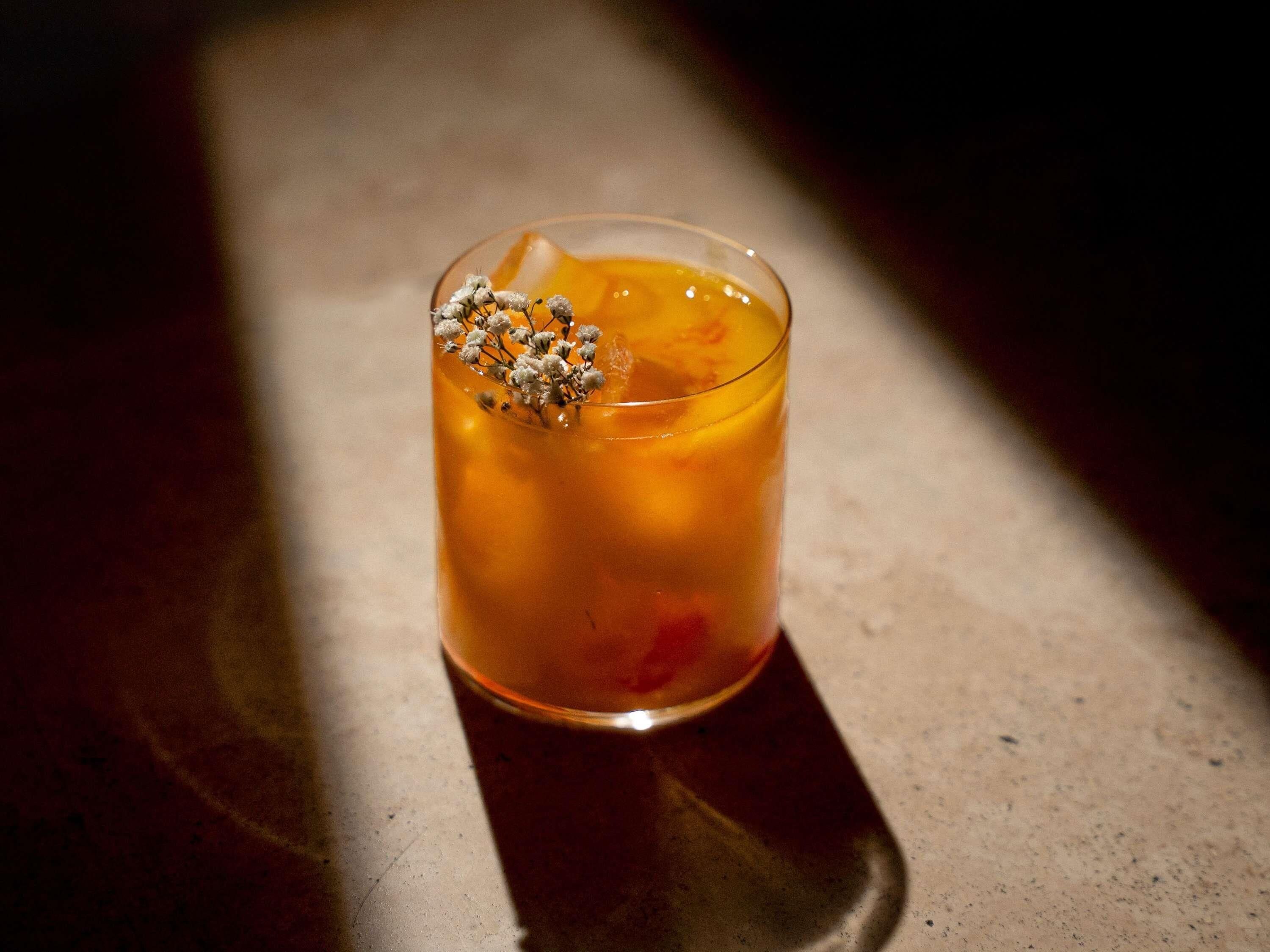 A glass with a clear liquid, possibly a cocktail, garnished with a flower and a small decorative element.