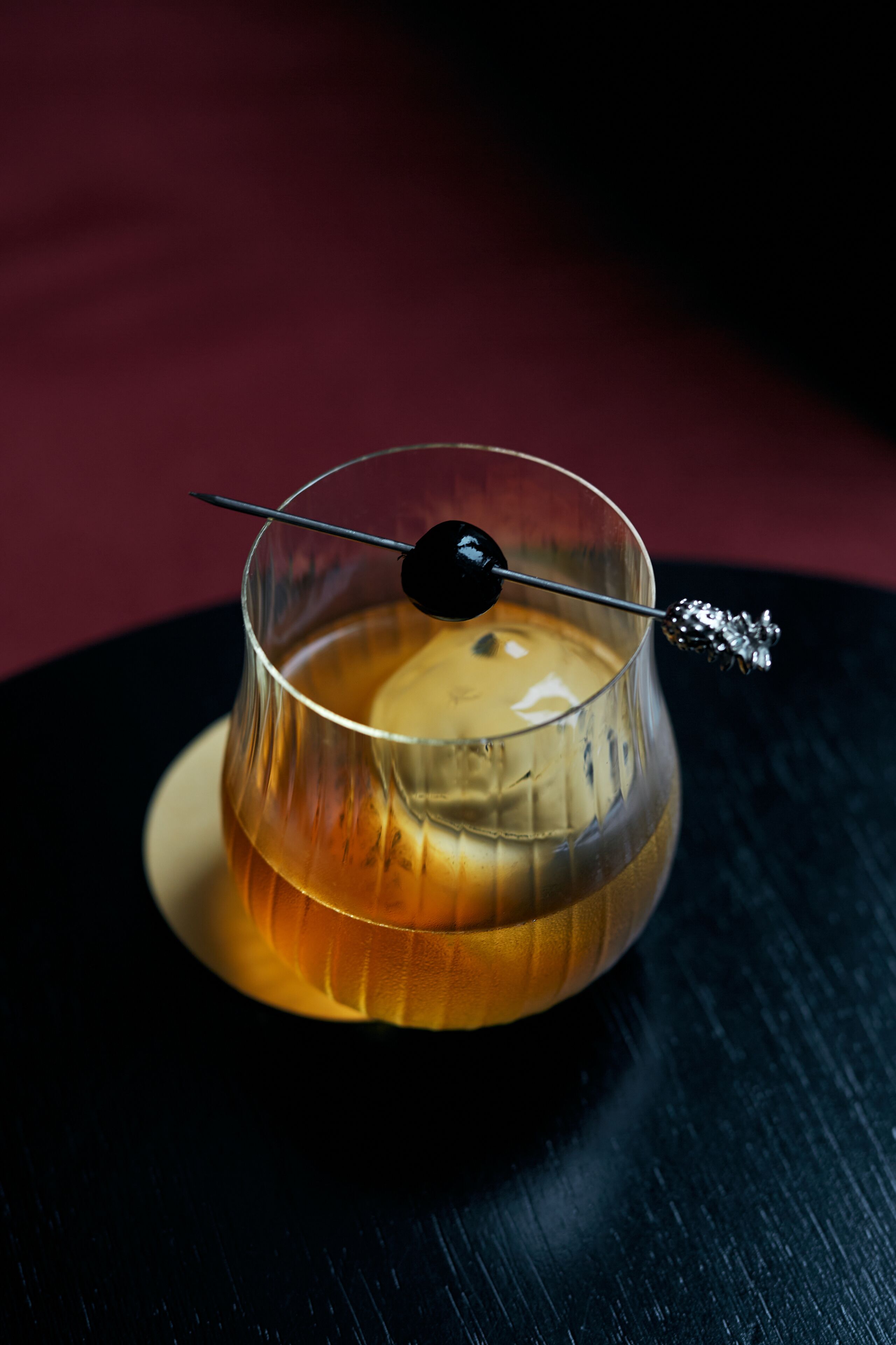 Un verre contenant un liquide doré, une sphère noire et un élément décoratif argenté, le tout posé sur une surface sombre.
