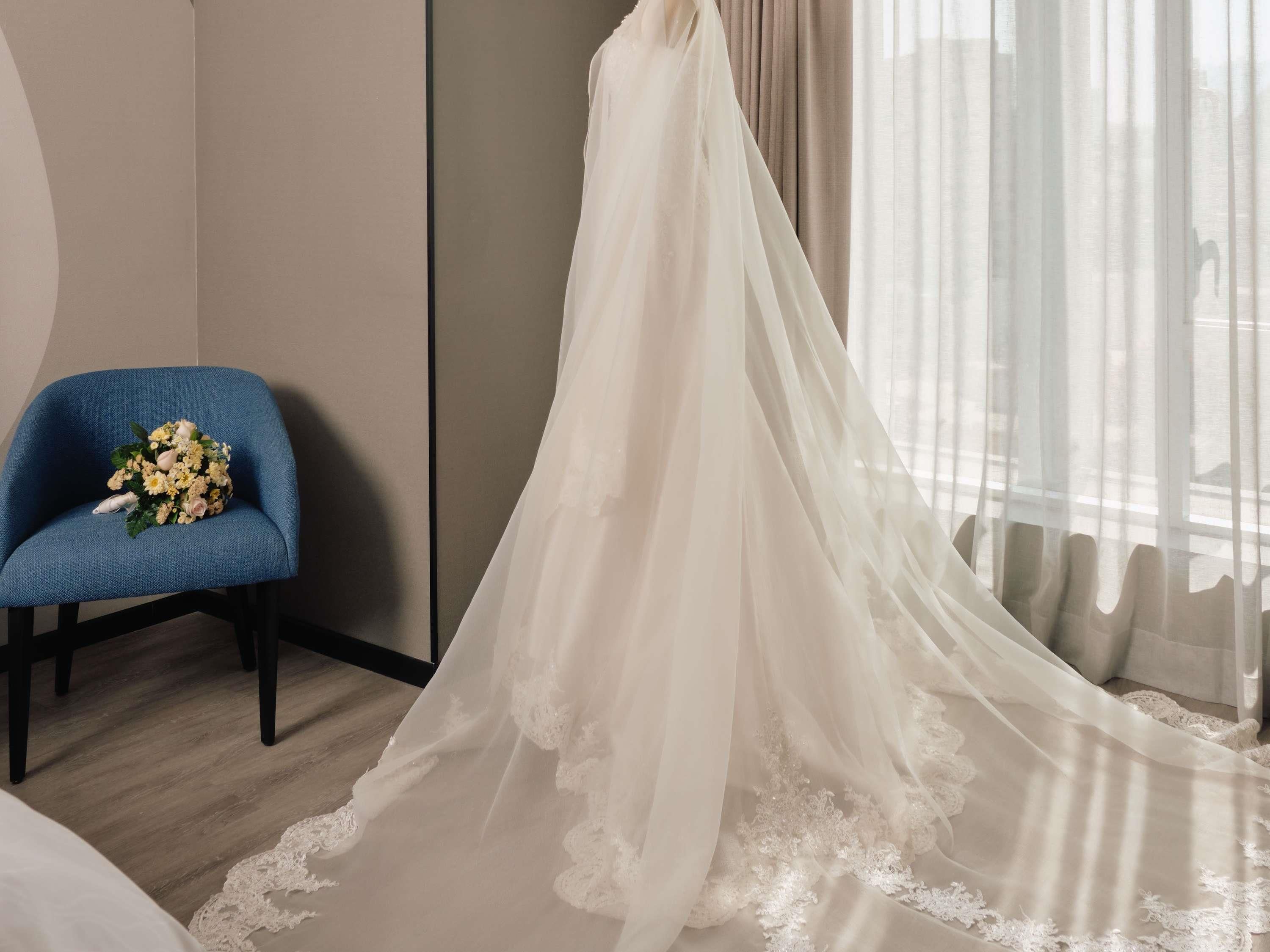 A room with a blue chair, a white wedding dress, and a bouquet.