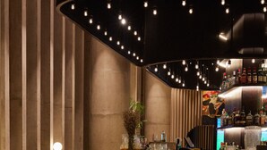 A bar area with a curved counter, bar stools, and a seating area with a table and chairs. - Pullman Lima San Isidro (Lima)