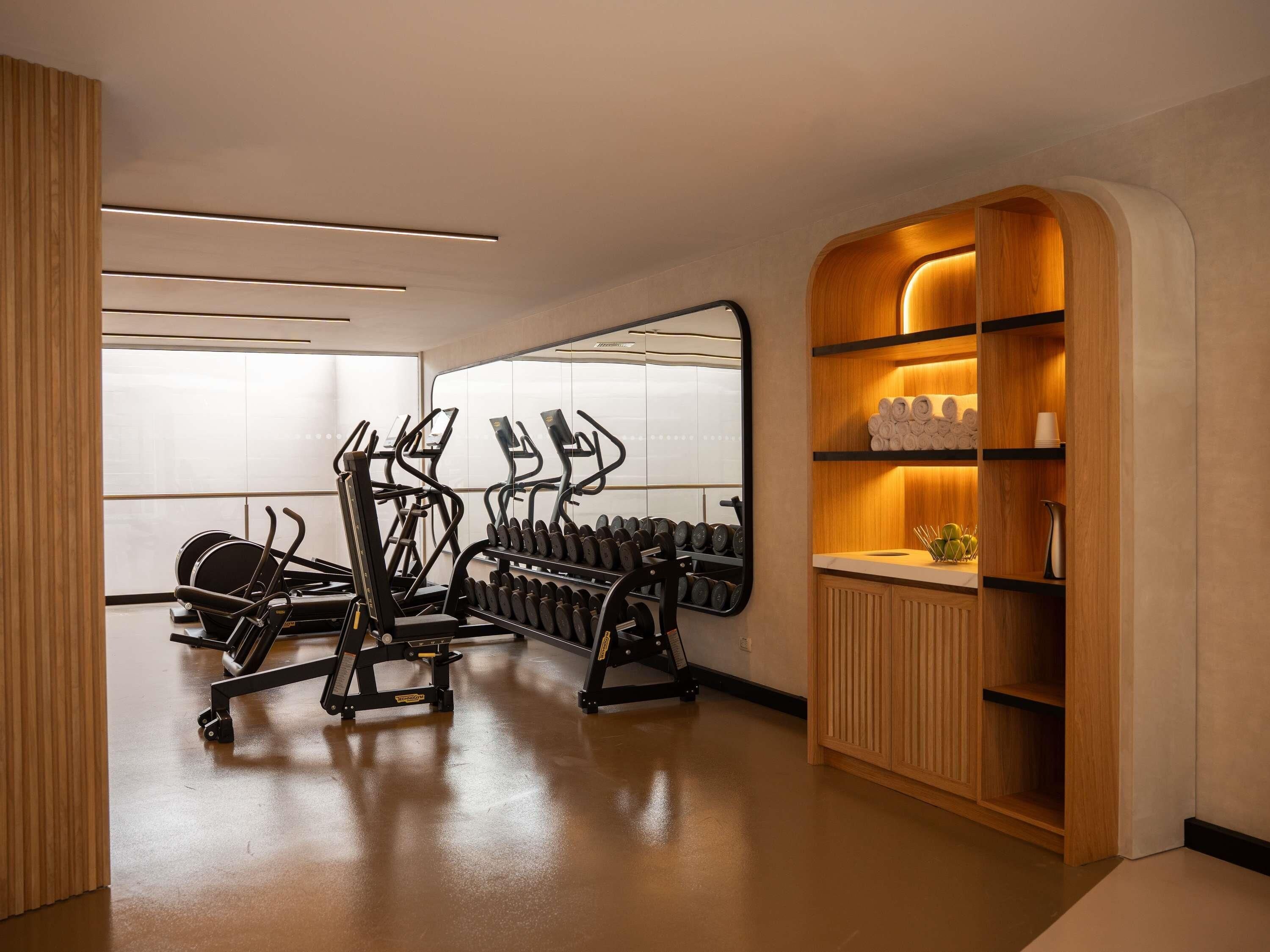 A modern gym with exercise equipment, a mirror, and a wooden vanity with towels.