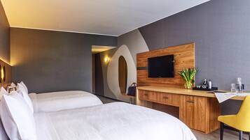 A modern hotel room with two beds, a wooden desk, a flat-screen TV, and a small desk lamp.