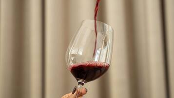 A hand holding a wine glass with red wine being poured into it.