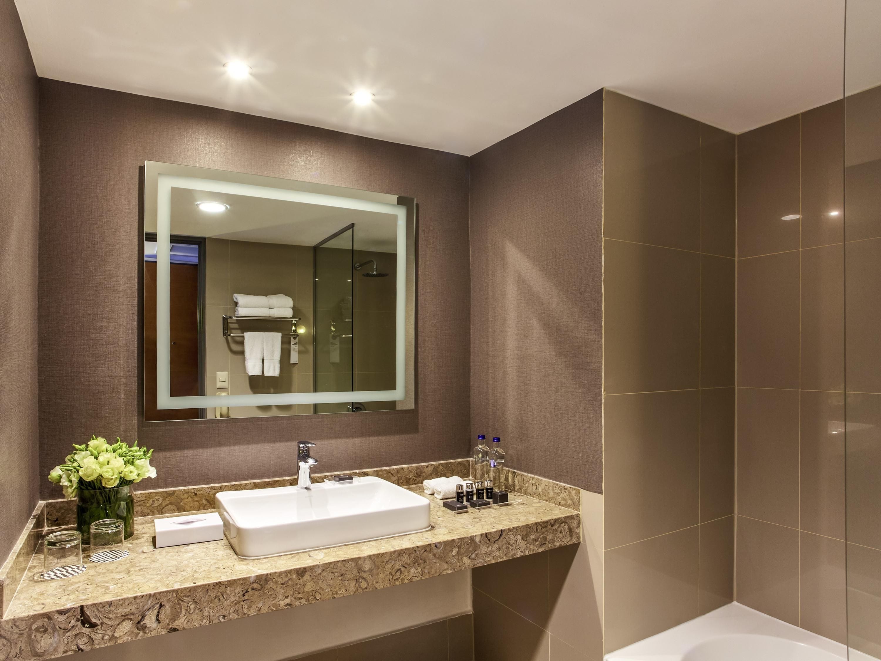Un baño moderno con un espejo grande, un lavamanos blanco y una ducha con mampara de vidrio.