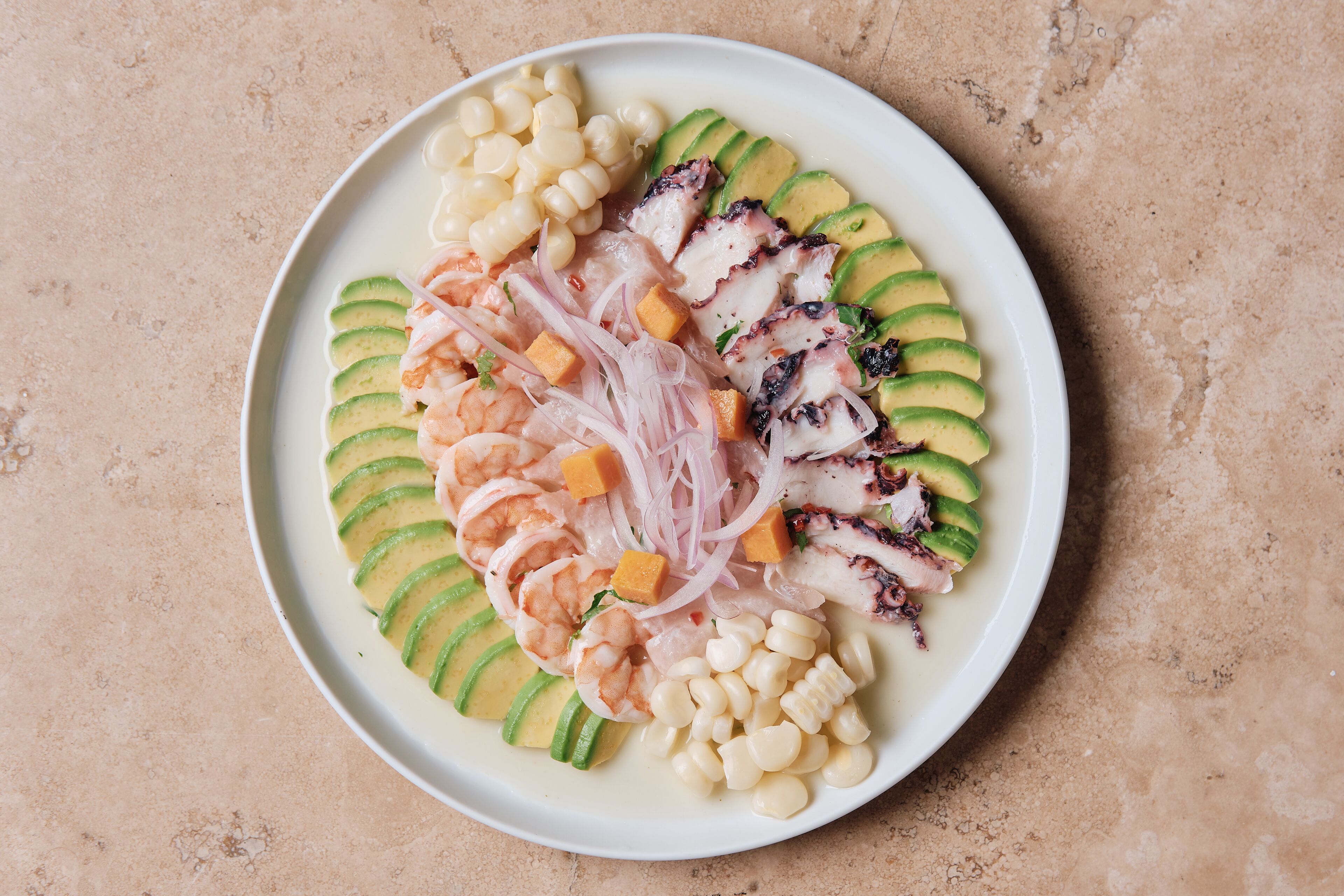 A plate of ceviche with shrimp, avocado, corn, and onions.