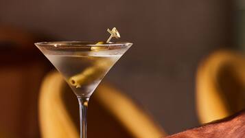 A martini glass with a lemon twist on a reflective surface, held by a hand.