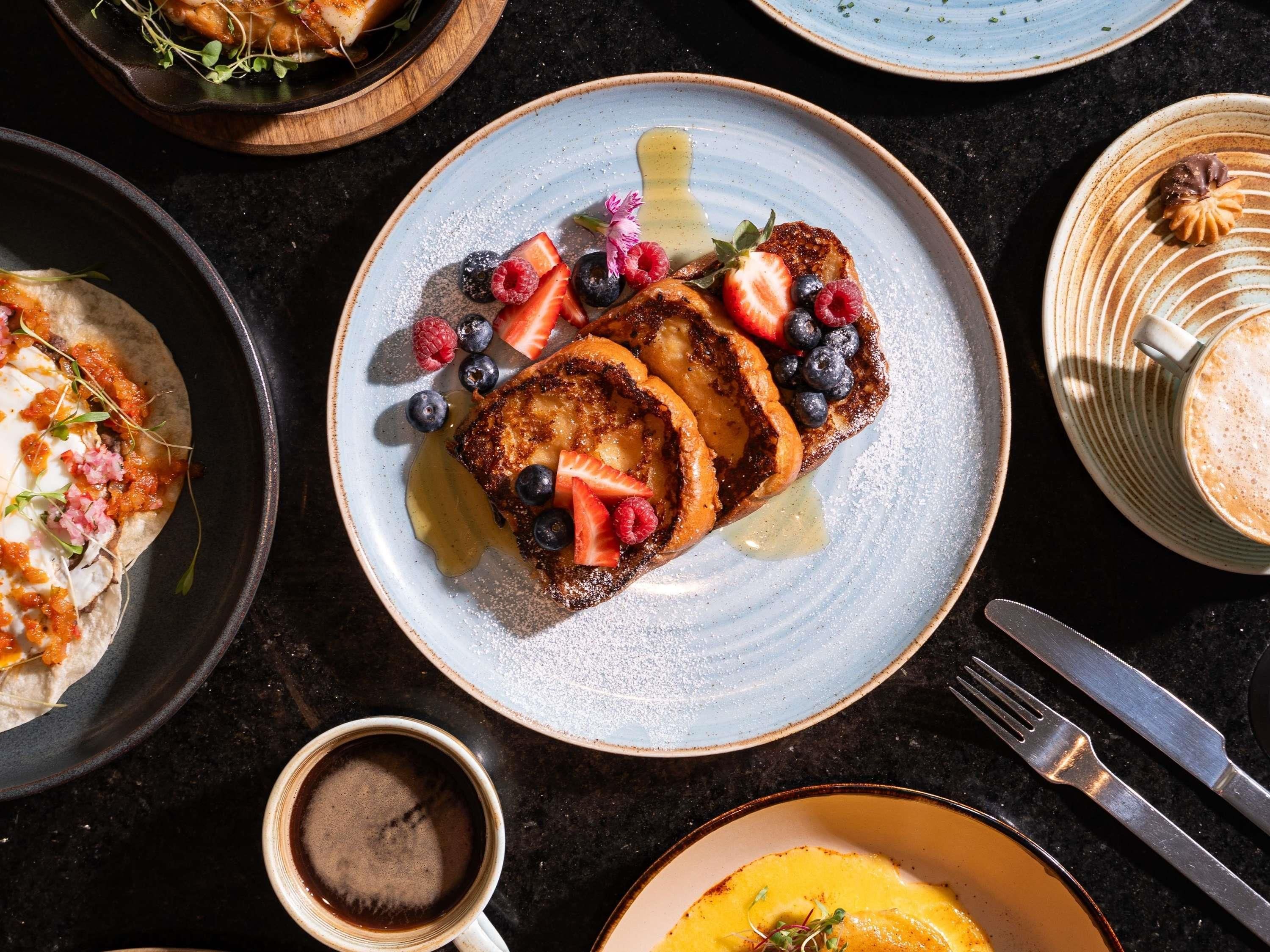 Une table dressée pour le petit-déjeuner avec des crêpes, des fruits rouges et du sirop.