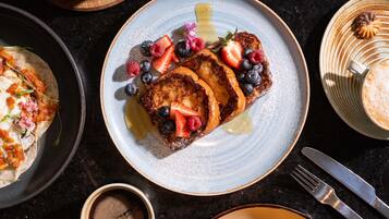Une table dressée pour le petit-déjeuner avec des crêpes, des fruits rouges et du sirop.