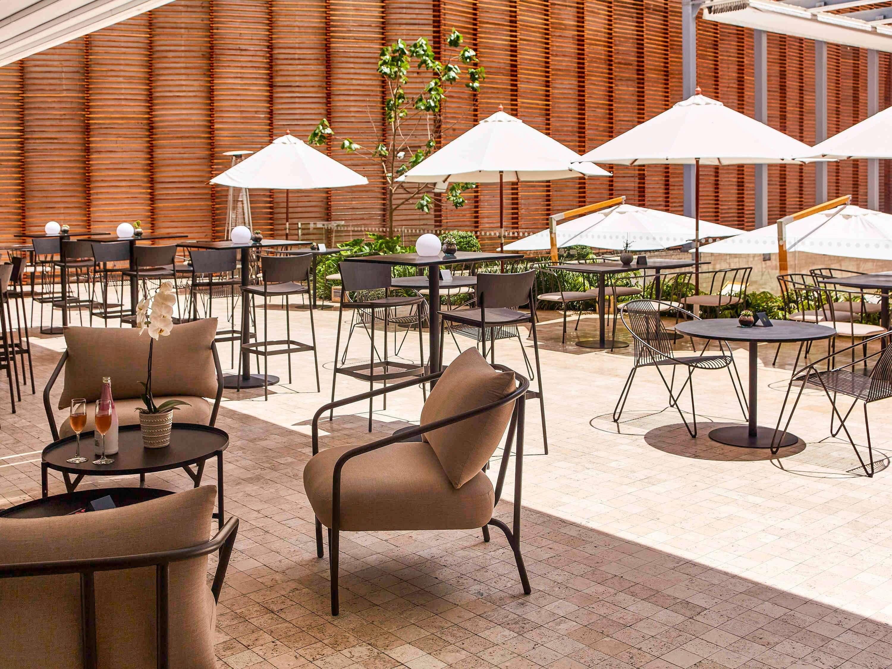 An outdoor seating area with tables and chairs, umbrellas, and a wooden wall in the background.