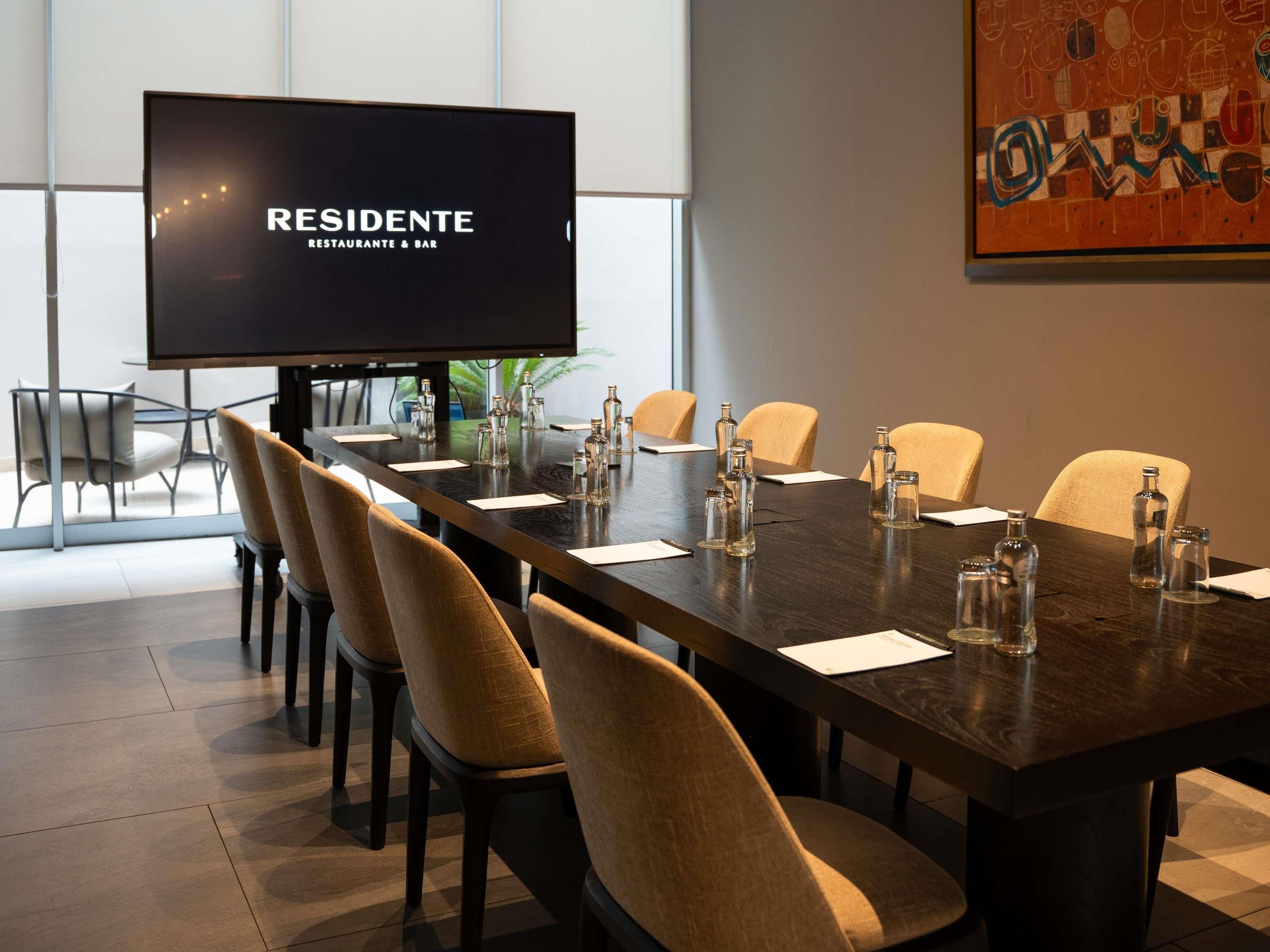 A conference room with a long table, chairs, a television screen, and a large abstract painting on the wall.