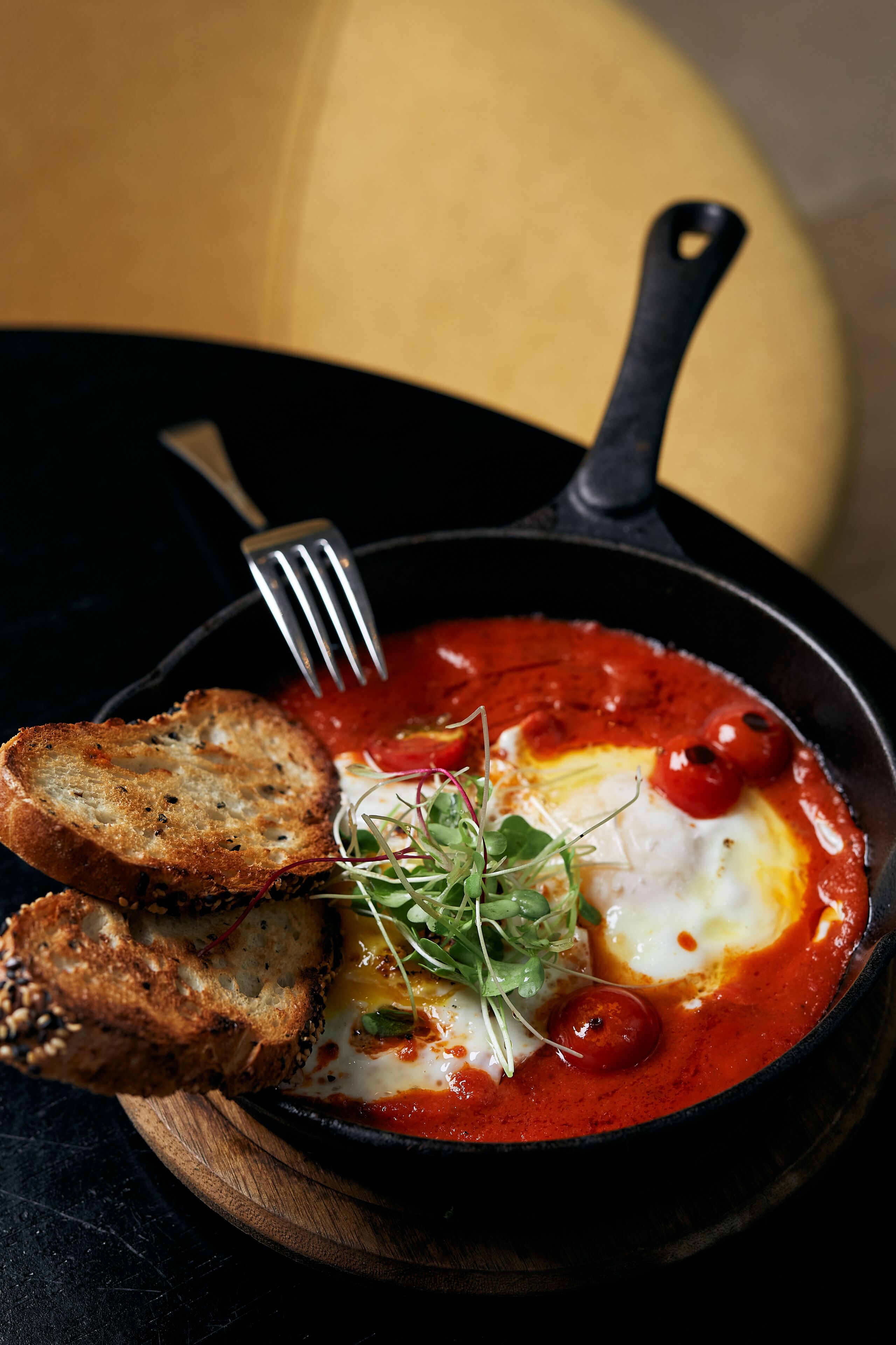 A skillet with a breakfast dish, including eggs and tomato sauce, accompanied by toasted bread.